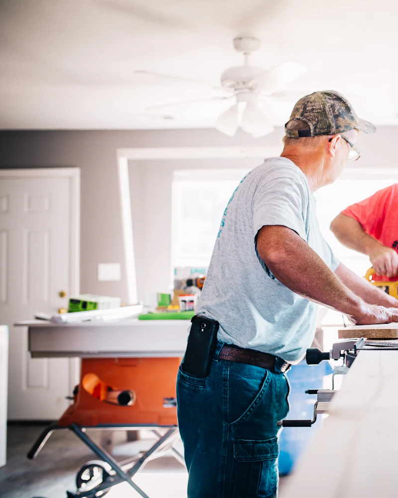 A carpenter working at a miter saw set up on a bench inside a house under renovation.